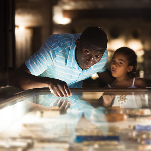 Male visitor and his little daughter visiting museum and looking at showcase with exhibits