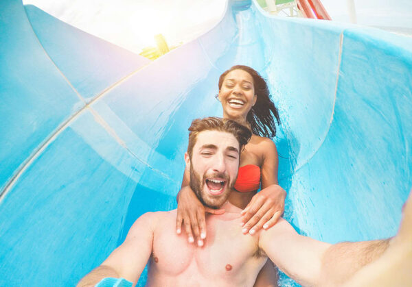 Young happy friends having fun in aqua park pipe during weekend Young happy friends having fun in aqua park pipe during weekend holidays - Crazy multi race couple taking selfie photo with funny faces - Summer vacation, travel and love concept